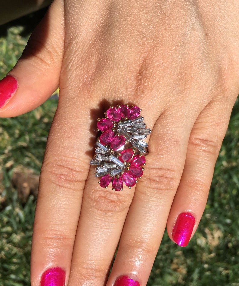 May include: A ring featuring a cluster of pink gemstones and baguette-cut diamonds set in a gold band.