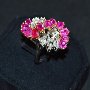 May include: A ring featuring a cluster of pink gemstones and baguette-cut diamonds set in a silver band.
