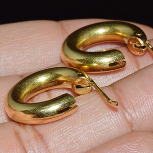 May include: A pair of gold hoop earrings with a hinged closure. The earrings are smooth and shiny.