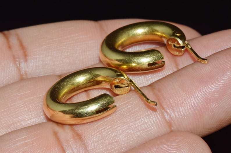 May include: A pair of gold hoop earrings with a hinged closure. The earrings are smooth and shiny.