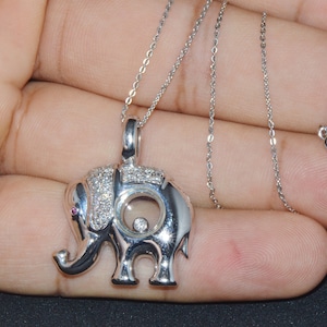 May include: A silver necklace with a diamond-encrusted elephant pendant. The elephant has a small pink stone for an eye and a round opening in its back that reveals a smaller diamond.