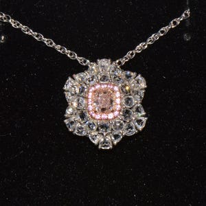 Puede incluir: Un collar de plata con un colgante que presenta una gran piedra preciosa rosa rodeada de piedras preciosas transparentes m&aacute;s peque&ntilde;as.