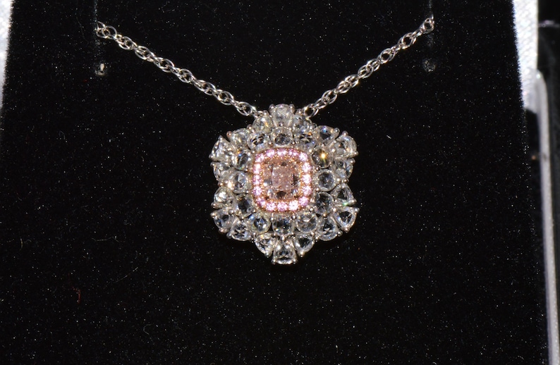 Puede incluir: Un collar de plata con un colgante que presenta una gran piedra preciosa rosa rodeada de piedras preciosas transparentes m&aacute;s peque&ntilde;as.