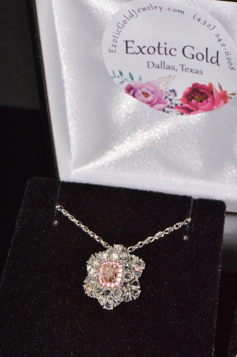 Puede incluir: Un collar de cadena de plata con un colgante de piedra preciosa rosa y blanca. El colgante tiene forma de flor con una piedra preciosa rosa grande en el centro rodeada de piedras preciosas blancas m&aacute;s peque&ntilde;as.