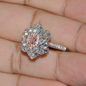 Puede incluir: Un anillo de plata con una gran piedra ovalada rosa y blanca rodeada de piedras blancas m&aacute;s peque&ntilde;as. El anillo est&aacute; engastado en un dise&ntilde;o con forma de flor.
