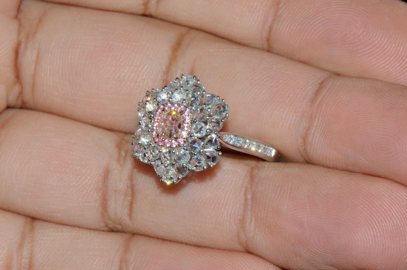 Puede incluir: Un anillo de plata con una gran piedra ovalada rosa y blanca rodeada de piedras blancas m&aacute;s peque&ntilde;as. El anillo est&aacute; engastado en un dise&ntilde;o con forma de flor.