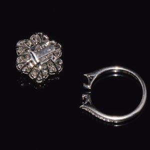 Puede incluir: Un anillo de plata con una piedra grande, redonda, similar a un diamante, engastada en un dise&ntilde;o con forma de flor. El anillo se muestra con el engaste retirado, revelando la banda de metal.