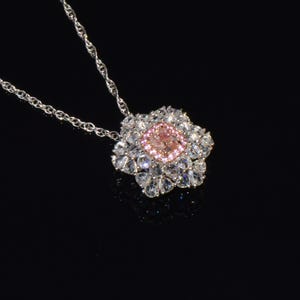 Puede incluir: Un collar de cadena de plata con un colgante que presenta una piedra preciosa rosa rodeada de piedras preciosas transparentes m&aacute;s peque&ntilde;as.
