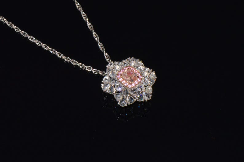 Puede incluir: Un collar de cadena de plata con un colgante que presenta una piedra preciosa rosa rodeada de piedras preciosas transparentes m&aacute;s peque&ntilde;as.