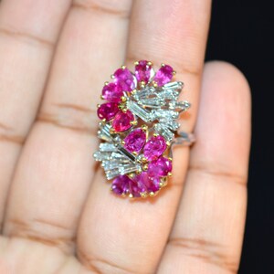 May include: A ring featuring a cluster of pink gemstones and baguette-cut diamonds set in white gold.