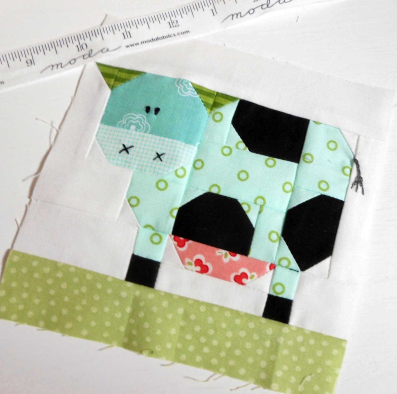 May include: A patchwork quilt block featuring a green, black, and pink cow with white polka dots. The cow is standing on a green and white polka dot background.