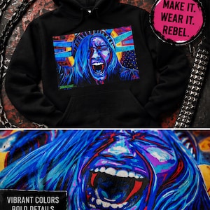 May include: Black hoodie featuring a vibrant, colorful graphic of a screaming face with blue hair. The design includes red, blue, and yellow accents. The text "MAKE IT. WEAR IT. REBEL." is on a pink circle. The bottom of the image reads "VIBRANT COLORS BOLD DETAILS."