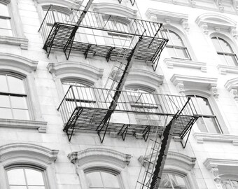 May include: A black and white photo of a building with a fire escape. The fire escape is made of metal and has a series of steps and landings. The building is made of brick and has a series of windows.