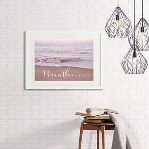 May include: A framed print with a photograph of a beach scene with a wave crashing on the shore. The text "Breathe..." is printed in pink on the sand.
