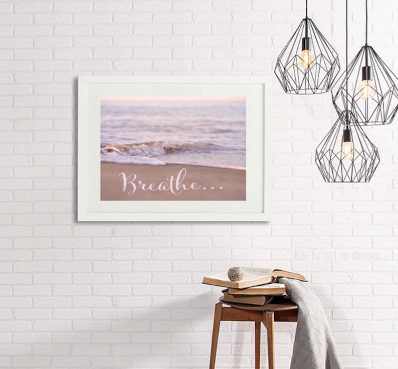 May include: A framed print with a photograph of a beach scene with a wave crashing on the shore. The text "Breathe..." is printed in pink on the sand.