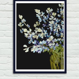 May include: A bouquet of blue and white flowers in a glass vase against a black background.