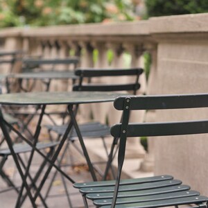 May include: A set of black metal bistro tables and chairs on a patio. The tables are round and have a black metal frame. The chairs are also black metal and have a slatted seat.