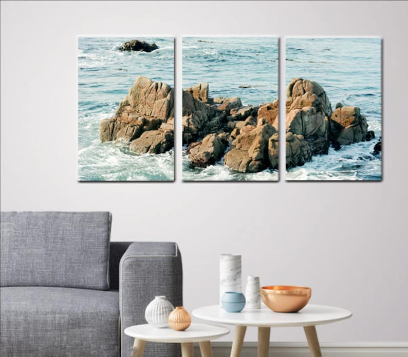 Może przedstawiać: Trzyczęściowy wydruk na pł&oacute;tnie przedstawiający krajobraz morski z dużymi skałami i rozbijającymi się falami. Skały są jasnobrązowe, a woda jest ciemnoniebieska.