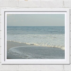 May include: A framed photograph of a beach scene with white foamy waves crashing on the shore. The water is a light blue color and the sky is a pale blue.
