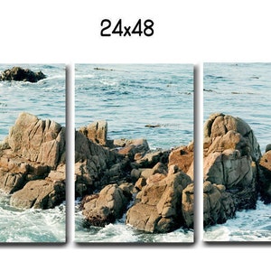 Może przedstawiać: Trzyczęściowy wydruk na pł&oacute;tnie przedstawiający malowniczy krajobraz morski z skalistymi wychodniami wynurzającymi się z błękitnej wody. Fale rozbijają się o skały, tworząc wrażenie ruchu i energii. Niebo jest jasnoniebieskie, a słońce świeci.