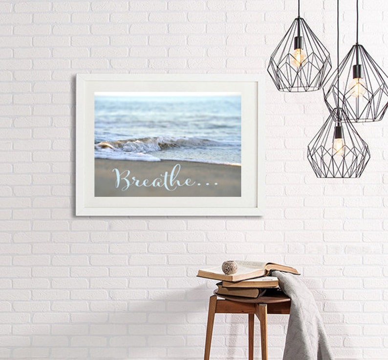 May include: A white framed print with a photograph of a wave crashing on a sandy beach. The text "Breathe..." is written in blue cursive on the sand.