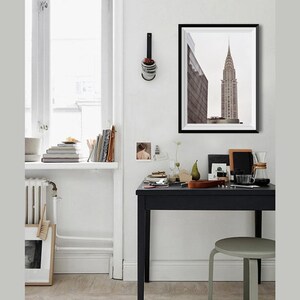 May include: A black and white photograph of a tall skyscraper in a city. The photograph is framed in a black frame and is hanging on a white wall.