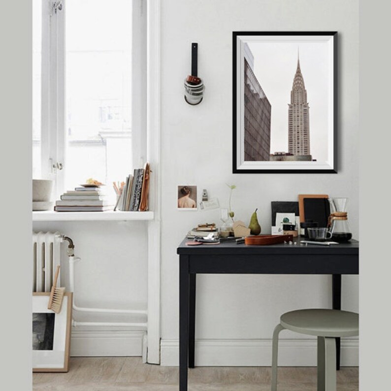 May include: A black and white photograph of a tall skyscraper in a city. The photograph is framed in a black frame and is hanging on a white wall.
