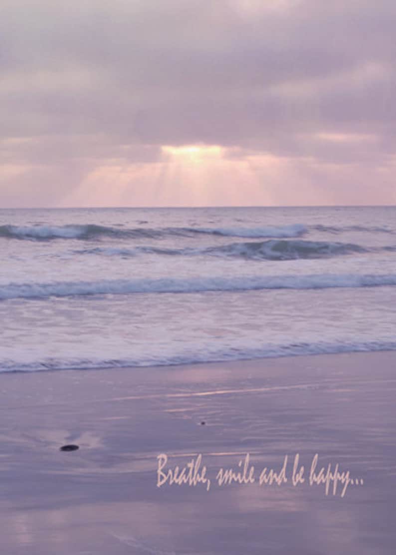 Pode incluir: Um suave p&ocirc;r do sol rosa e roxo sobre um oceano calmo com ondas que rolam suavemente para uma praia de areia. O texto "Breathe, smile and be happy..." est&aacute; escrito na areia.
