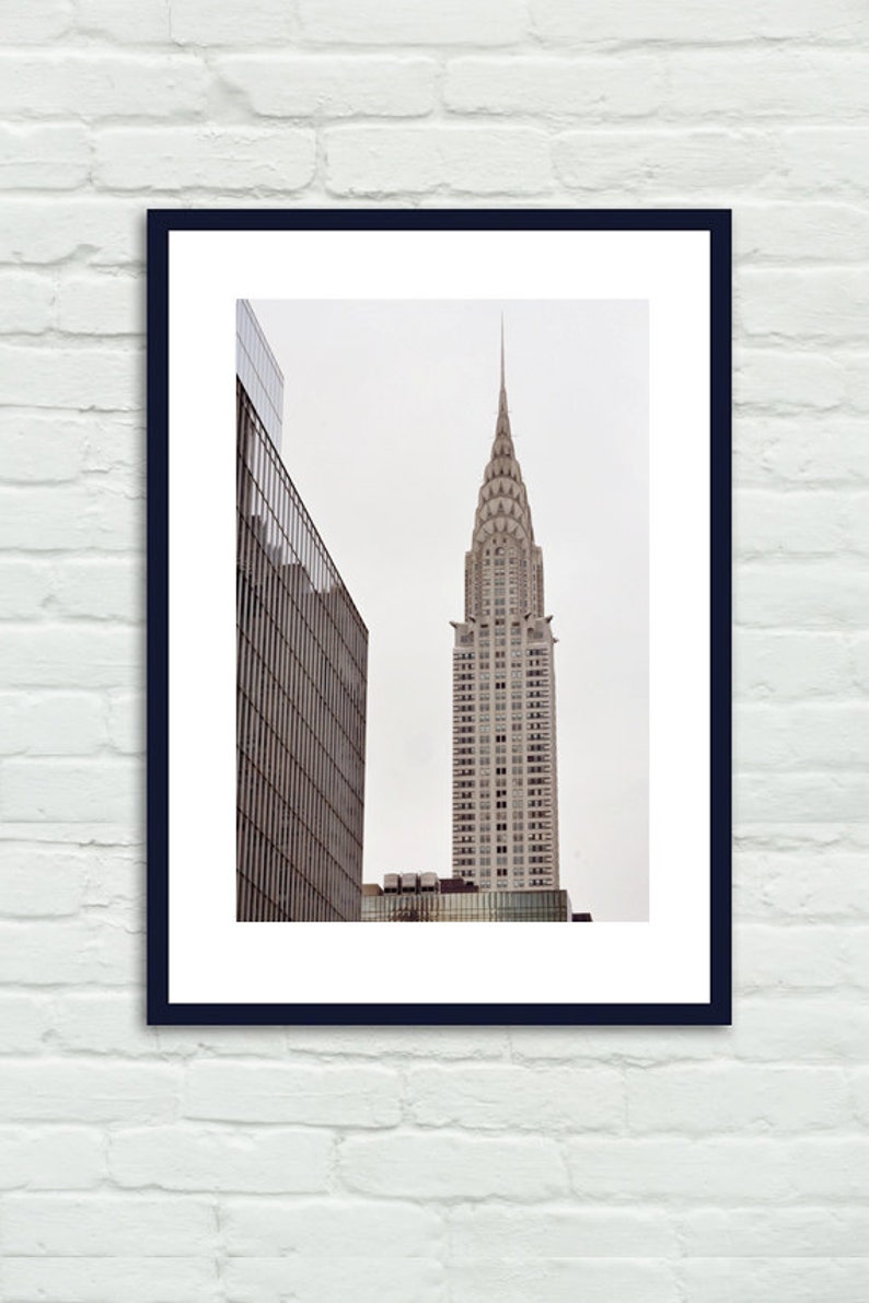 May include: A black and white photograph of a tall, pointed skyscraper with a decorative top. The building is in the center of the image and is surrounded by other buildings.