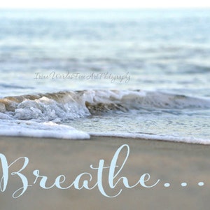 May include: A close-up of a foamy wave crashing on a sandy beach. The word "Breathe..." is written in light blue cursive on the sand.