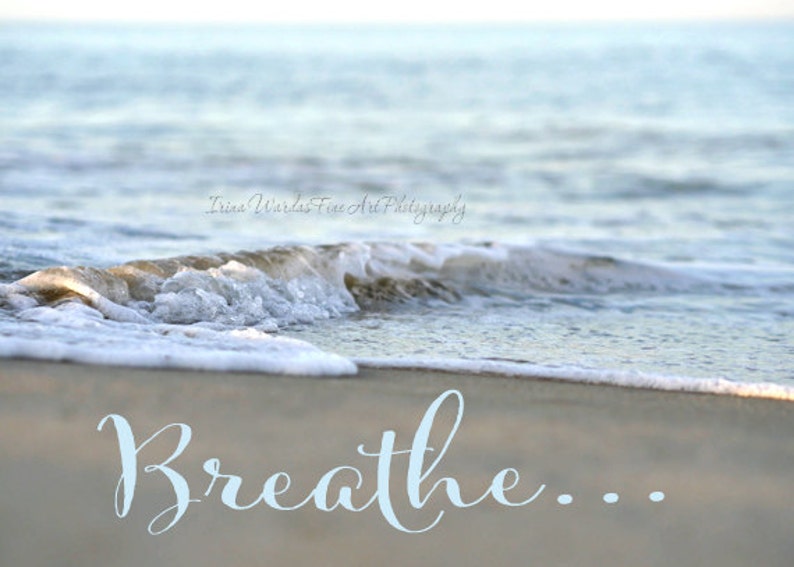 May include: A close-up of a foamy wave crashing on a sandy beach. The word "Breathe..." is written in light blue cursive on the sand.