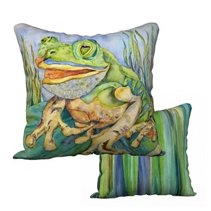 Könnte beinhalten: Ein grüner Frosch mit einem breiten Lächeln sitzt auf einem grünen Blatt mit grün-blau gestreiften Schilf im Hintergrund. Der Frosch ist in Aquarelltechnik dargestellt. Dies ist ein Dekokissen mit einem Froschmotiv.