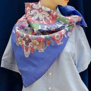 May include: A blue silk scarf with a colorful floral pattern. The scarf is folded and draped around a mannequin's neck.
