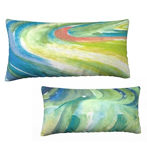 Könnte beinhalten: Zwei dekorative Kissen mit abstrakten Aquarelldesigns in Blautönen, Grün- und Gelbtönen. Das größere Kissen hat ein runderes Design, während das kleinere Kissen ein fließenderes Design hat.