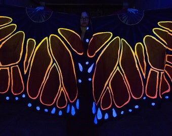May include: A pair of black butterfly wings with orange and yellow accents and blue dots. The wings are made of fabric and are glowing in the dark.