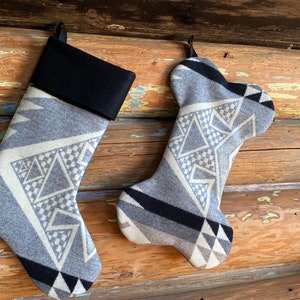 May include: Two Christmas stockings with a geometric pattern in shades of gray, black, and cream. One stocking is a traditional shape, and the other is shaped like a dog bone. Both have a black cuff and a loop for hanging.