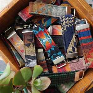 May include: A wooden box overflowing with colorful fabric key fobs. The key fobs feature various geometric patterns in shades of red, blue, orange, and green. Each fob has a silver-colored metal clasp.