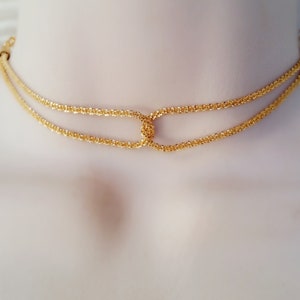 May include: A gold-toned double-strand choker necklace with a delicate, woven chain design. The necklace features a simple, oval-shaped clasp in the center.