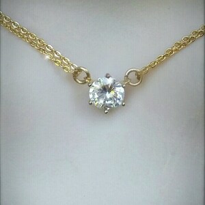 Puede incluir: Un delicado collar de cadena dorada con un solo colgante de piedra redonda transparente grande.