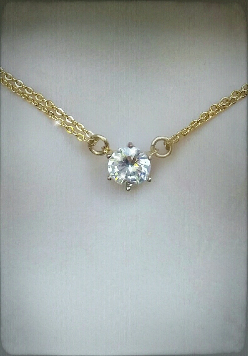 Puede incluir: Un delicado collar de cadena dorada con un solo colgante de piedra redonda transparente grande.