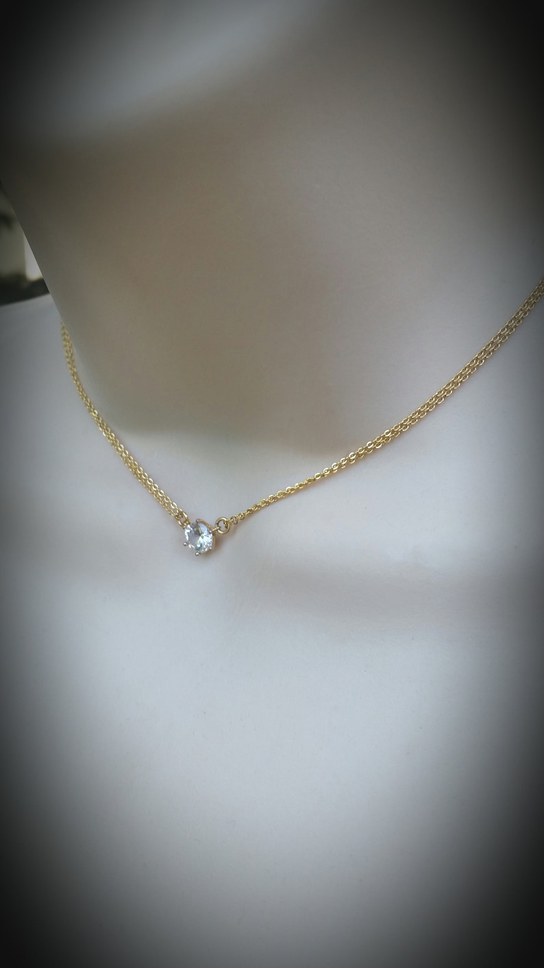 Puede incluir: Un delicado collar de cadena de oro con un solo colgante de cristal transparente.