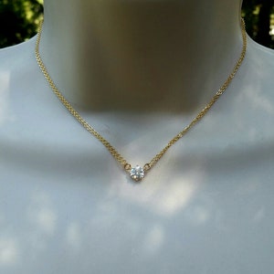 Puede incluir: Un delicado collar de cadena de oro con un solo colgante de piedra preciosa redonda transparente.