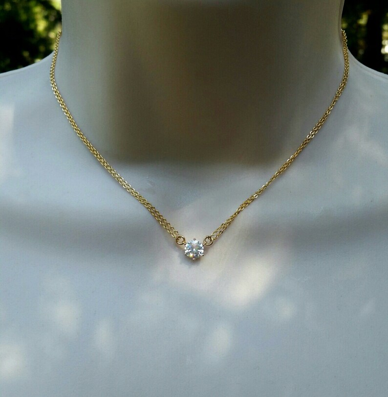 Puede incluir: Un delicado collar de cadena de oro con un solo colgante de piedra preciosa redonda transparente.