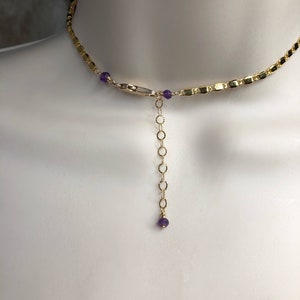 May include: Gold-toned necklace with a delicate chain design. The necklace features small, round purple gemstones and a chain extender. The necklace is displayed on a mannequin.