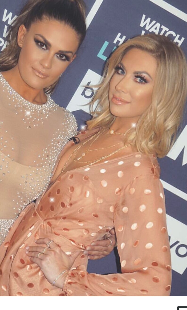 May include: Two women posing for a photo. The woman on the left is wearing a sheer, beaded top. The woman on the right is wearing a peach-colored polka dot blouse with a gold necklace.
