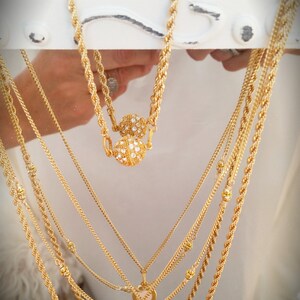 May include: A set of six gold necklaces with various chain styles. One necklace features a round pendant with a pink stone and a smaller pearl charm. Another necklace has two round pendants with clear stones.