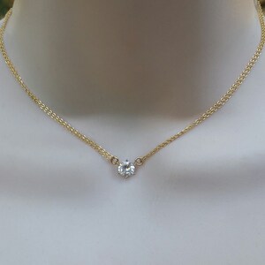 Puede incluir: Un delicado collar de cadena de oro con un solo colgante de piedra preciosa redonda transparente.