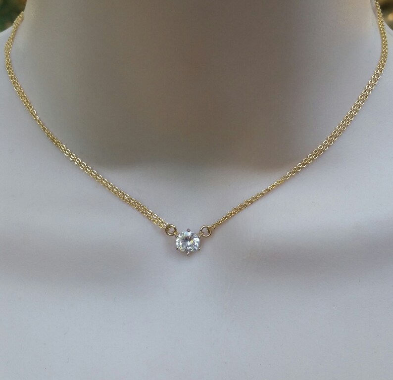 Puede incluir: Un delicado collar de cadena de oro con un solo colgante de piedra preciosa redonda transparente.