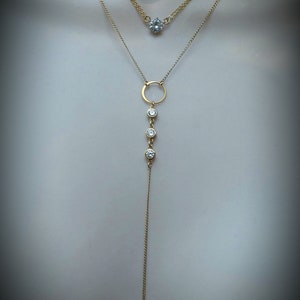 Puede incluir: Un collar de cadena de oro con un peque&ntilde;o colgante redondo y una cadena m&aacute;s larga con un colgante circular y tres piedras redondas m&aacute;s peque&ntilde;as.