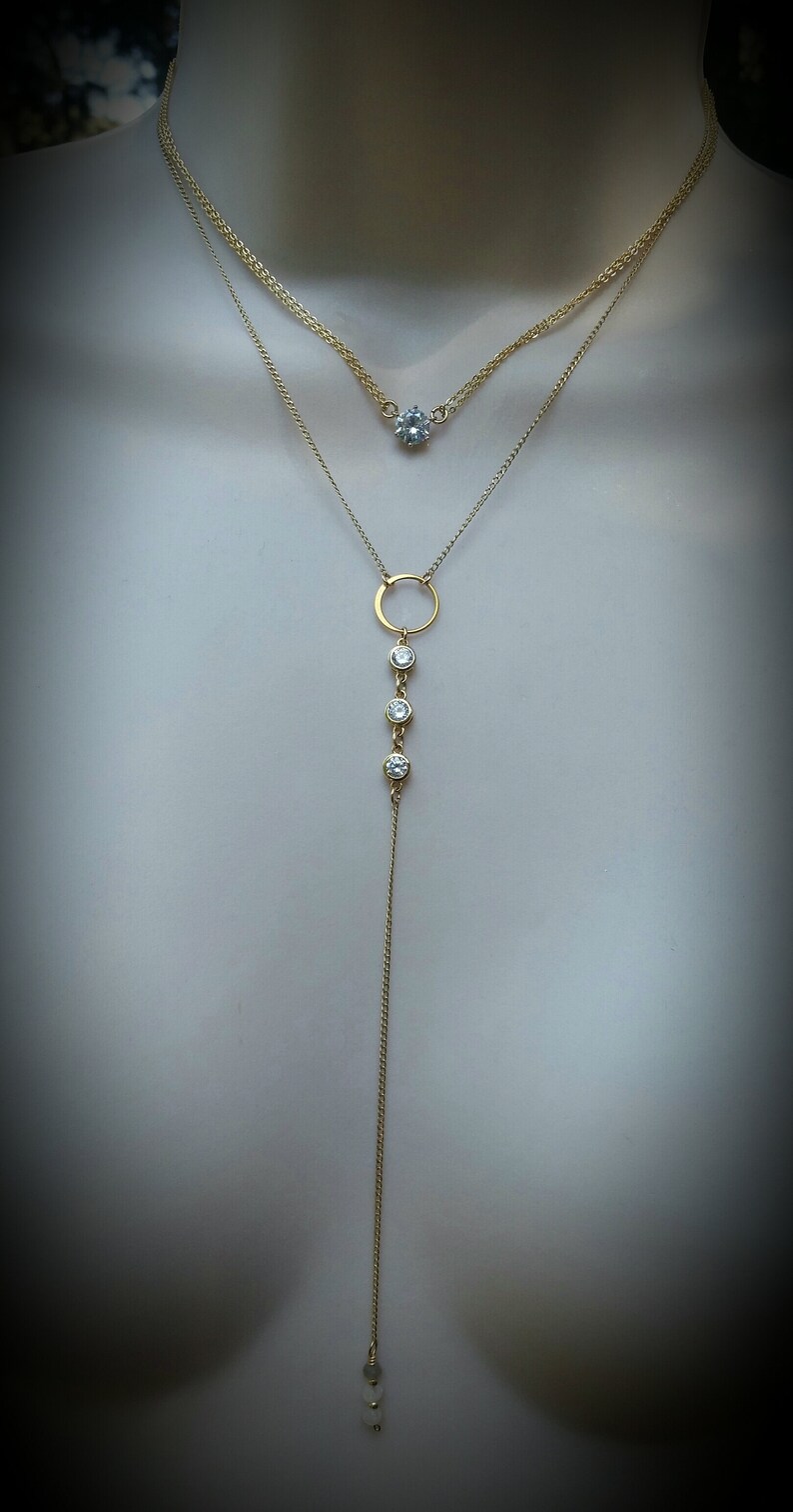 Puede incluir: Un collar de cadena de oro con un peque&ntilde;o colgante redondo y una cadena m&aacute;s larga con un colgante circular y tres piedras redondas m&aacute;s peque&ntilde;as.